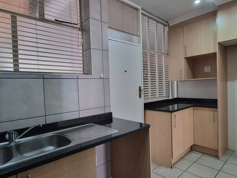 A functional kitchen featuring laminate cabinetry, granite countertops, a double stainless steel sink, and tiled flooring with natural light from large windows.