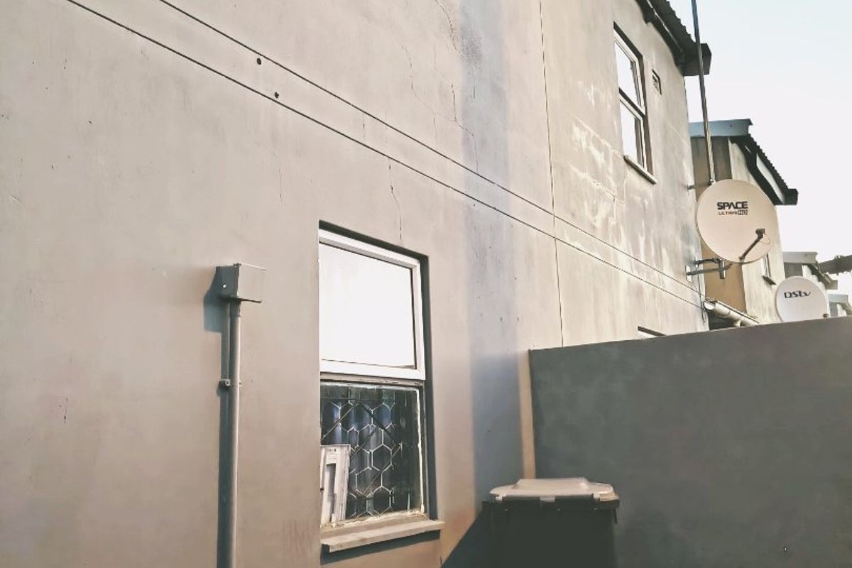Rear exterior view of the townhouse showing the plastered facade, windows, satellite dish installation, and boundary wall.