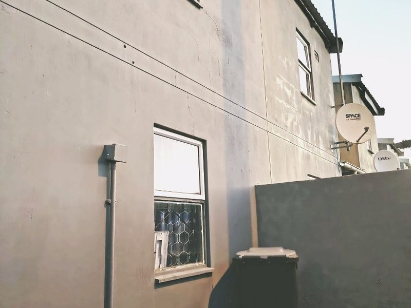 Rear exterior view of the townhouse showing the plastered facade, windows, satellite dish installation, and boundary wall.