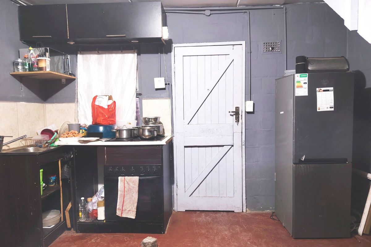 A basic kitchen area featuring a built-in oven, hob, sink, and upper cabinetry with exposed electrical conduit and unfinished wall surfaces.