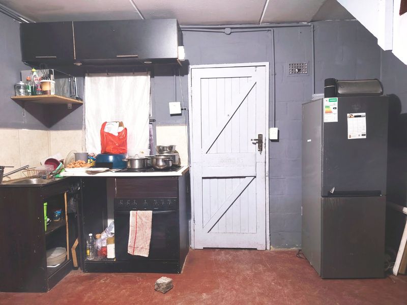 A basic kitchen area featuring a built-in oven, hob, sink, and upper cabinetry with exposed electrical conduit and unfinished wall surfaces.