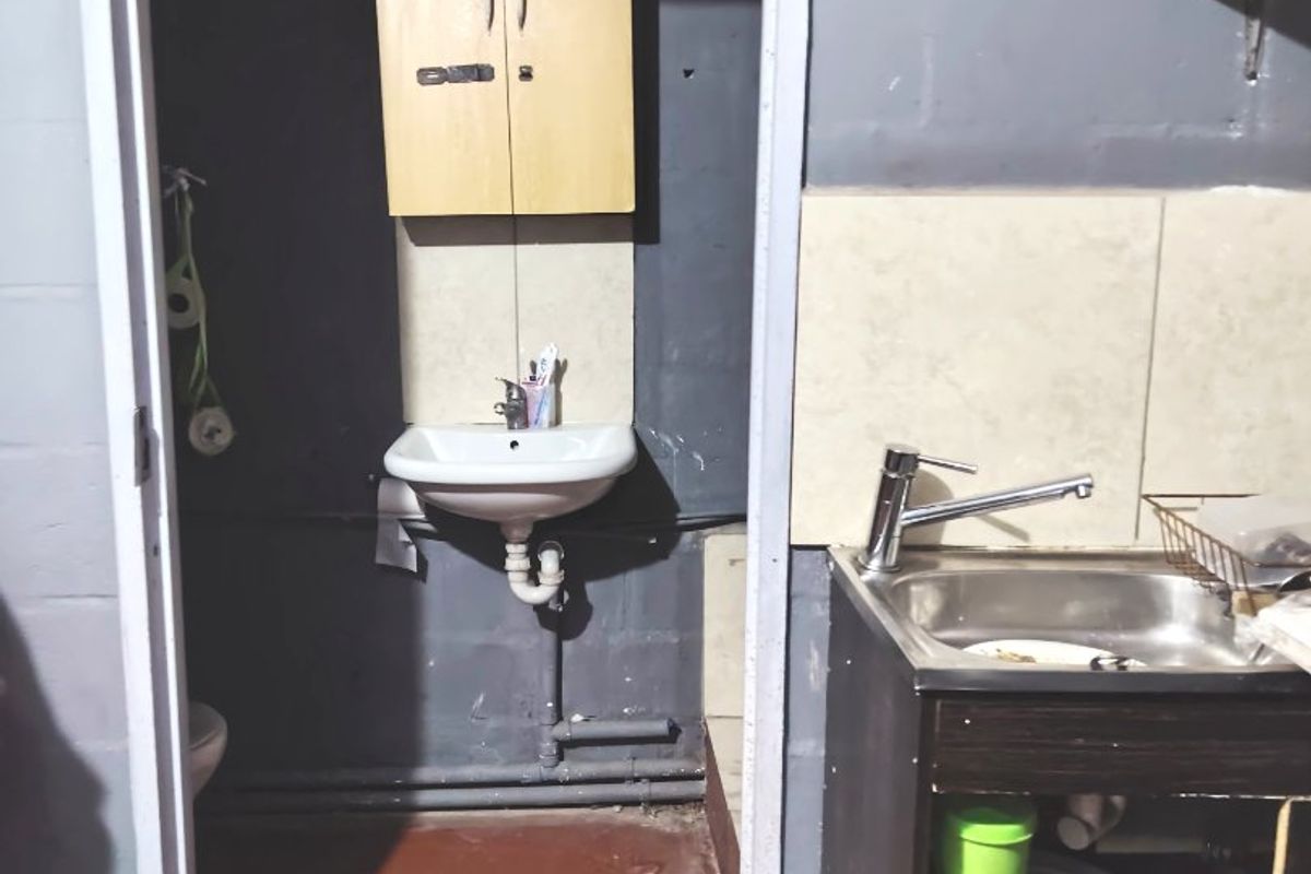 A functional scullery area featuring a stainless steel sink, wall-mounted basin, and basic cabinetry, requiring cosmetic updates to improve the overall finish.