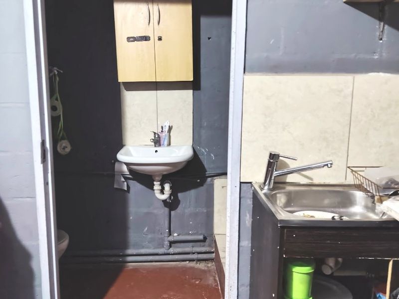 A functional scullery area featuring a stainless steel sink, wall-mounted basin, and basic cabinetry, requiring cosmetic updates to improve the overall finish.