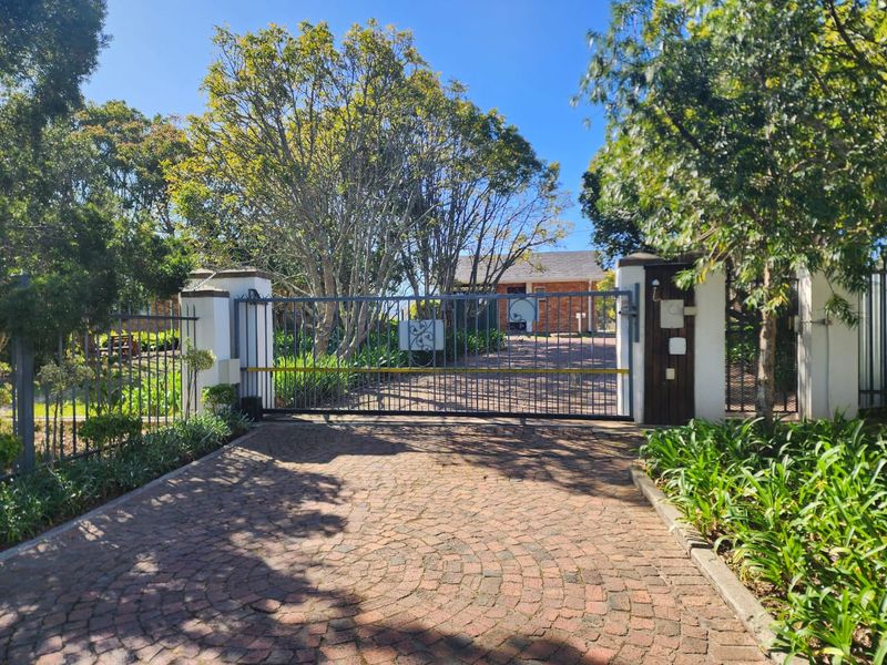 A secure front entrance featuring an automated sliding gate, brick paved driveway, and established landscaping leading to the property.