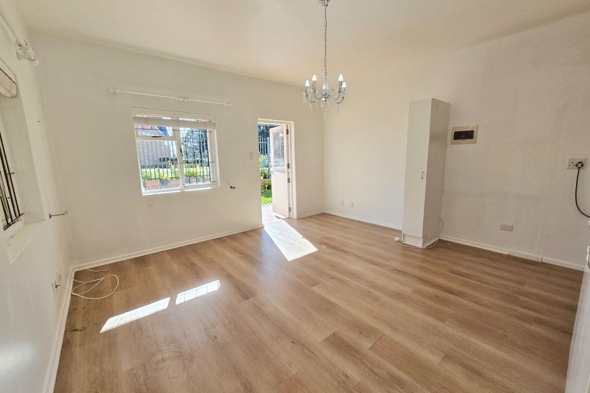A bright, empty living room featuring light wood-look laminate flooring, a decorative crystal chandelier, and a built-in storage cupboard with direct access to the outdoors.