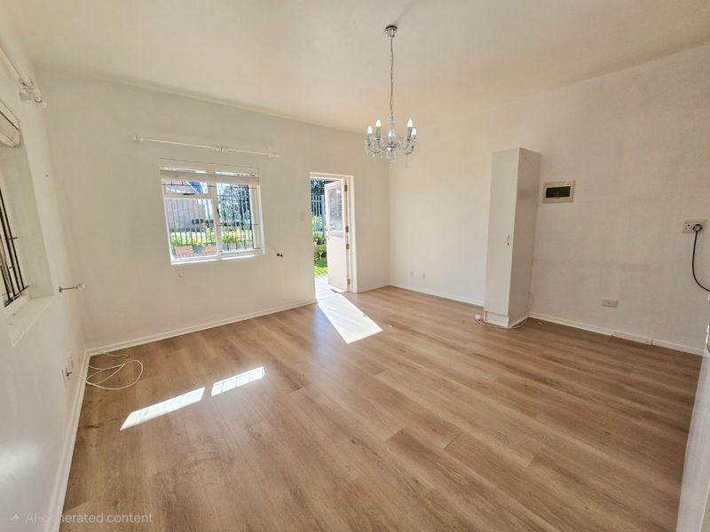 A bright, empty living room featuring light wood-look laminate flooring, a decorative crystal chandelier, and a built-in storage cupboard with direct access to the outdoors.
