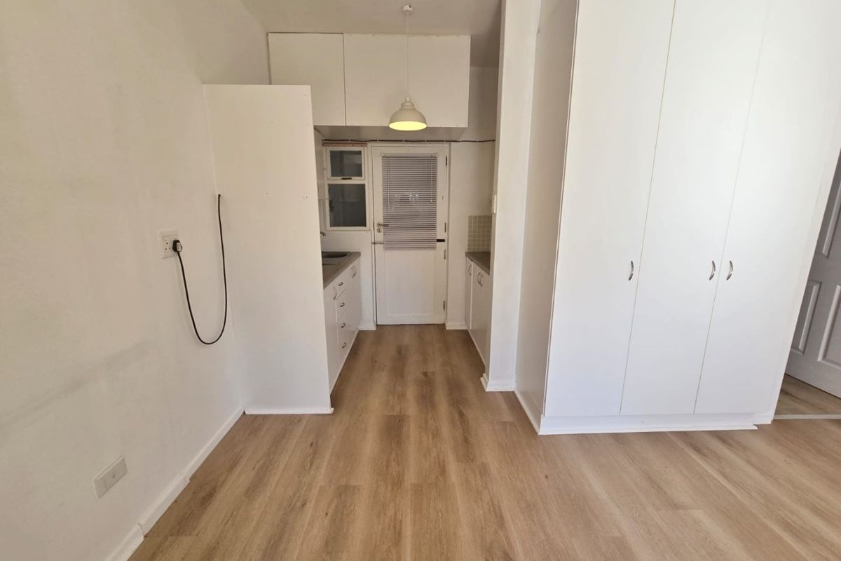 A clean, minimalist kitchen area featuring light wood-look laminate flooring, ample built-in white cabinetry, and a functional layout with direct exterior access.