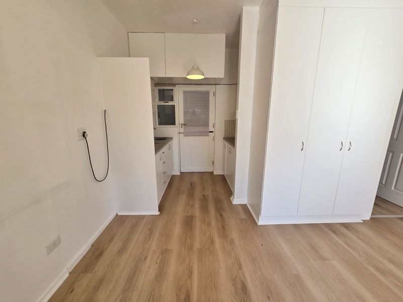 A clean, minimalist kitchen area featuring light wood-look laminate flooring, ample built-in white cabinetry, and a functional layout with direct exterior access.