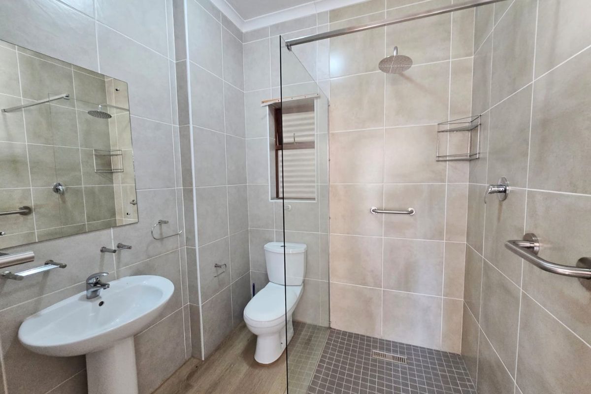 Modern bathroom featuring a walk-in shower with glass screen, pedestal washbasin, and neutral floor-to-ceiling tiling.