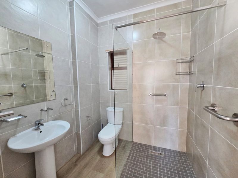 Modern bathroom featuring a walk-in shower with glass screen, pedestal washbasin, and neutral floor-to-ceiling tiling.