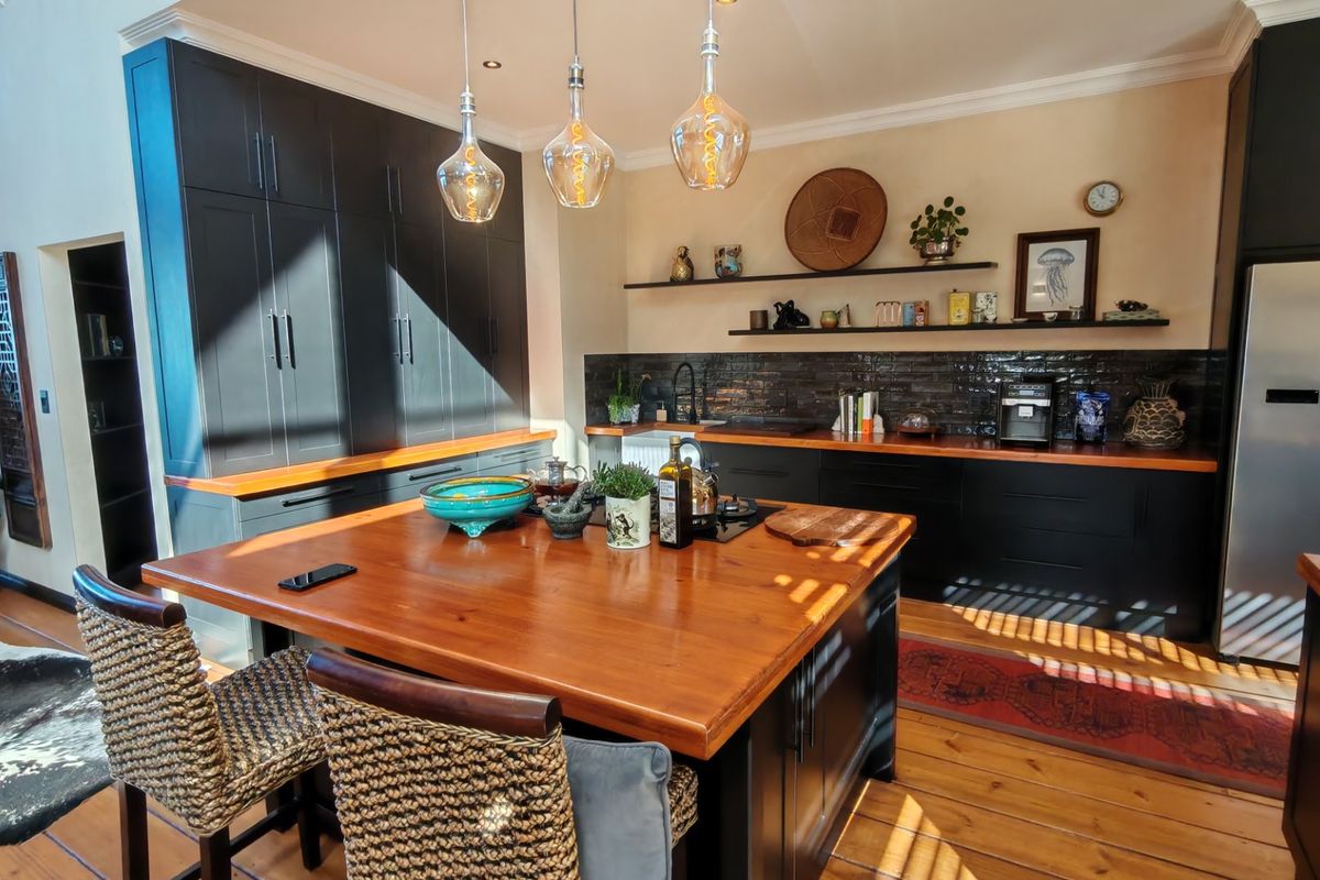 Modern kitchen featuring dark cabinetry, warm wooden countertops, a central island, and stylish subway tile backsplash, creating a sophisticated and functional culinary space.