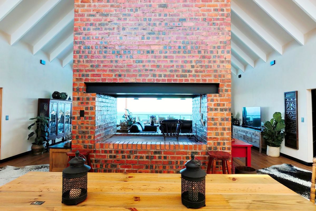 Spacious living area featuring a prominent double-sided exposed brick fireplace and high vaulted ceilings with exposed rafters, creating an open and airy atmosphere.