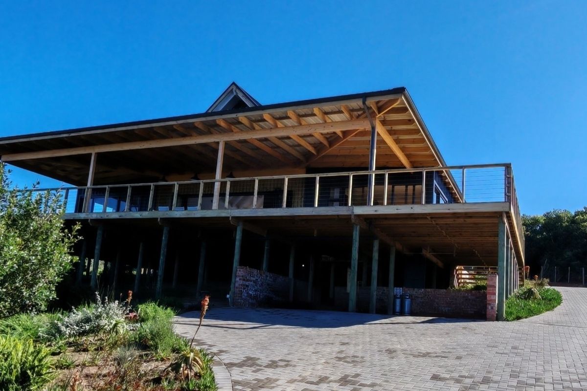 A spacious elevated timber deck with cable railings, overlooking a paved driveway and landscaped garden area.