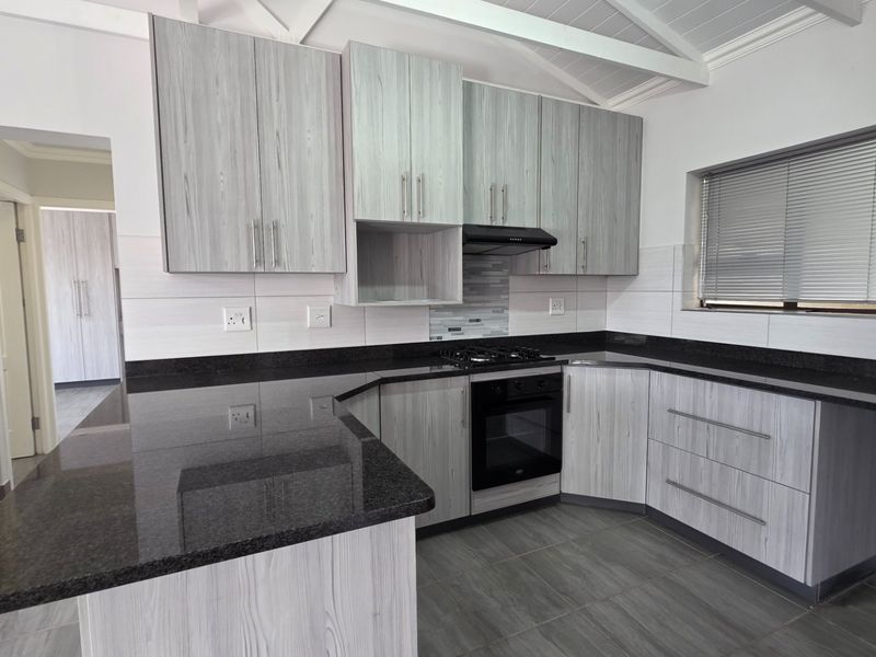 Modern kitchen featuring light wood-grain cabinetry, dark granite countertops, built-in oven, gas hob, and vaulted ceilings with tiled flooring.