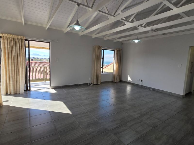 Spacious open-plan living area featuring exposed white timber trusses, modern tiled flooring, and direct access to a balcony with scenic views.