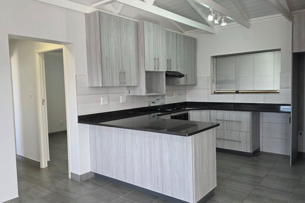 Modern kitchen featuring light wood-grain cabinetry, dark granite countertops, tiled flooring, and an exposed beam ceiling with track lighting.