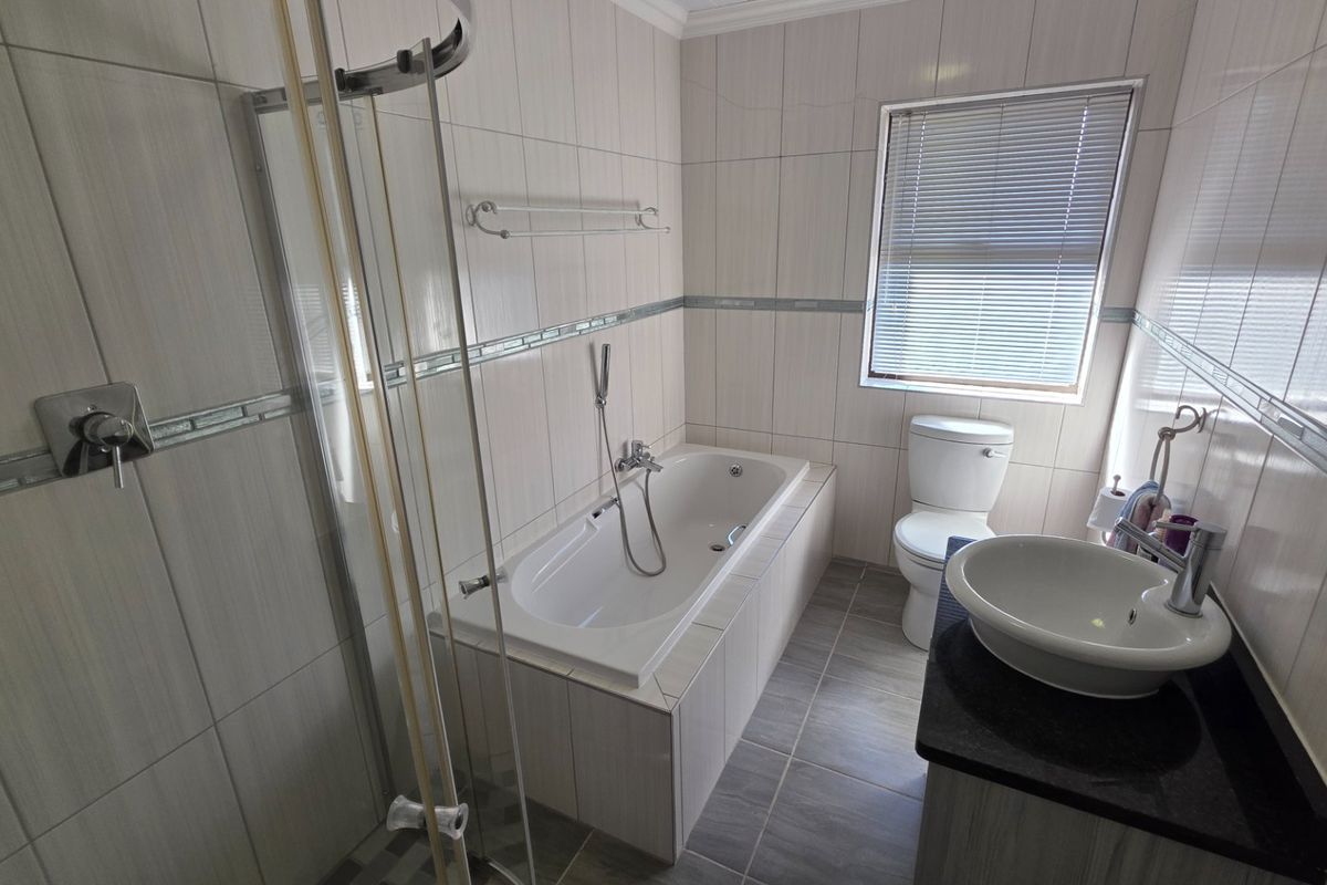 A clean, functional bathroom featuring a built-in bathtub, separate shower enclosure, vessel sink vanity, and neutral wall tiling.