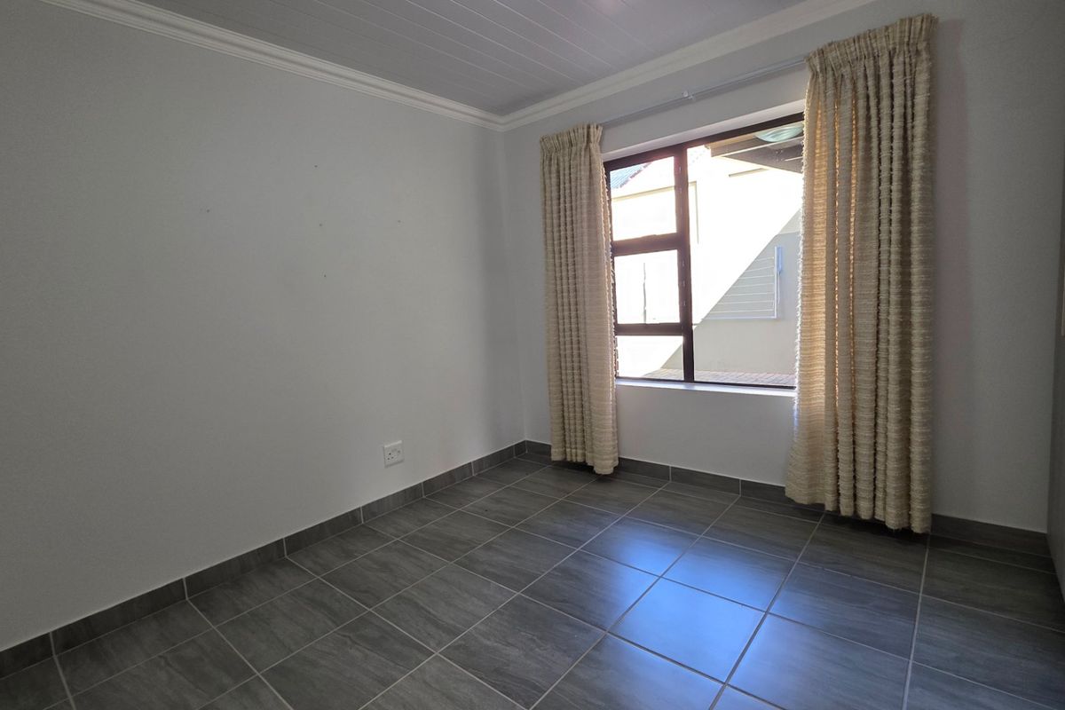A clean, empty bedroom featuring modern grey floor tiles, built-in cupboards, and a tongue and groove ceiling with cornice detailing.