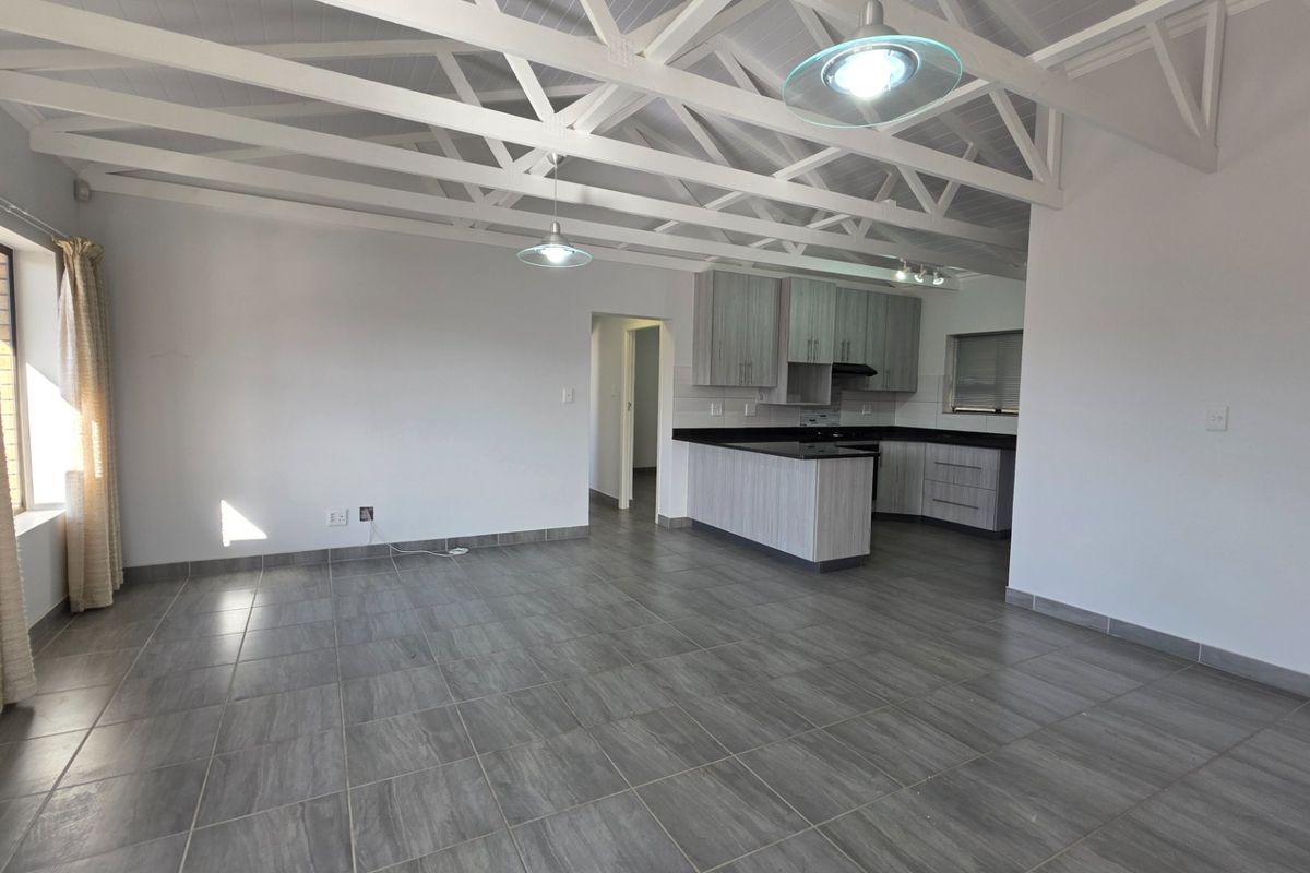 Spacious open-plan living area featuring exposed white roof trusses, modern grey tiled flooring, and a contemporary kitchen with stone countertops.