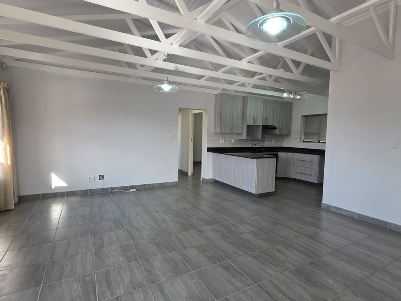 Spacious open-plan living area featuring exposed white roof trusses, modern grey tiled flooring, and a contemporary kitchen with stone countertops.