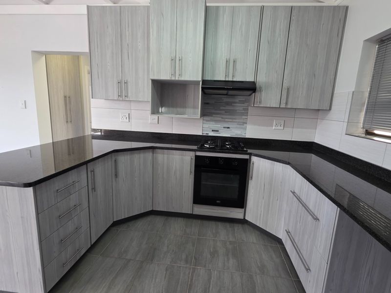 Modern kitchen featuring light wood-grain cabinetry, dark granite countertops, built-in gas hob, oven, and extractor fan with neutral tiled flooring.
