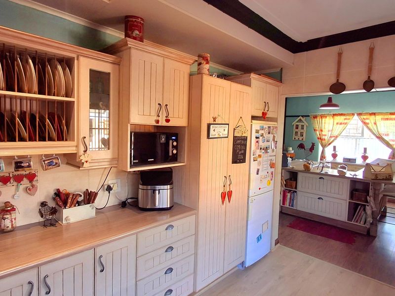 A functional kitchen featuring light-toned built-in cabinetry, laminate countertops, and a tiled backsplash, with an open-plan layout leading into an adjacent dining area.