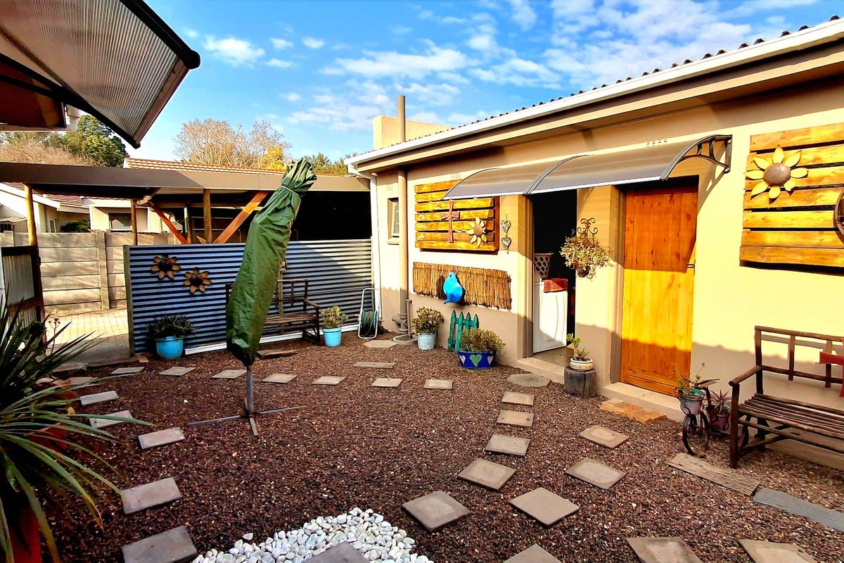 A rear courtyard area featuring gravel landscaping, paved stepping stones, a timber entrance door, and protective awning over the doorway.