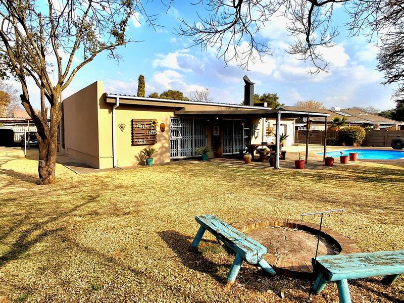 Rear view of the house featuring a swimming pool, covered patio area, and a built-in brick fire pit in the garden.