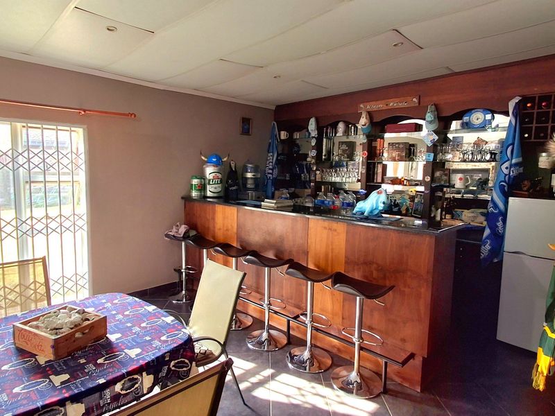 A dedicated home bar area featuring a built-in wooden counter, shelving, and tiled flooring, providing a functional space for entertaining.