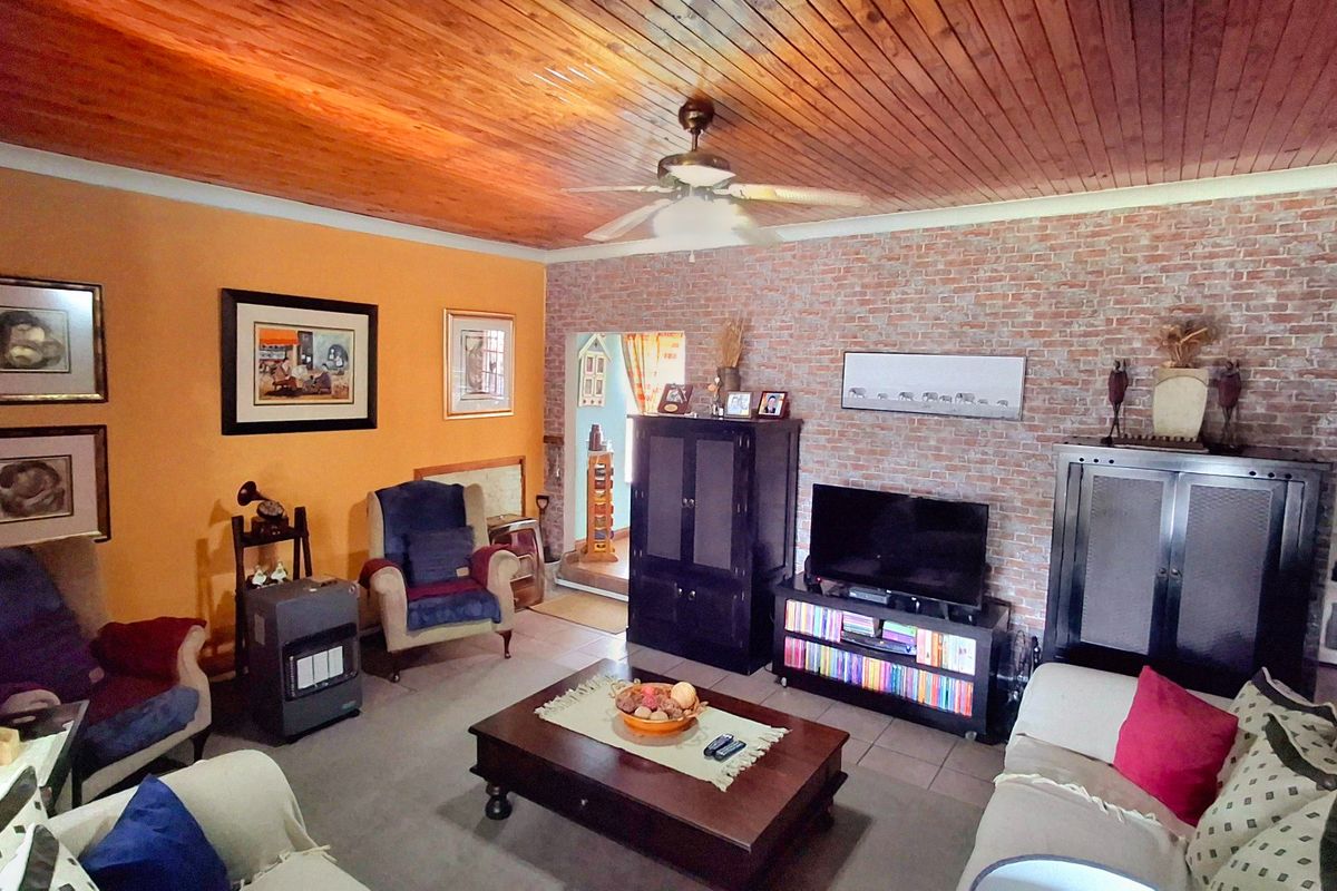 Spacious living room featuring a warm timber tongue and groove ceiling, an exposed brick feature wall, and neutral tiled flooring.