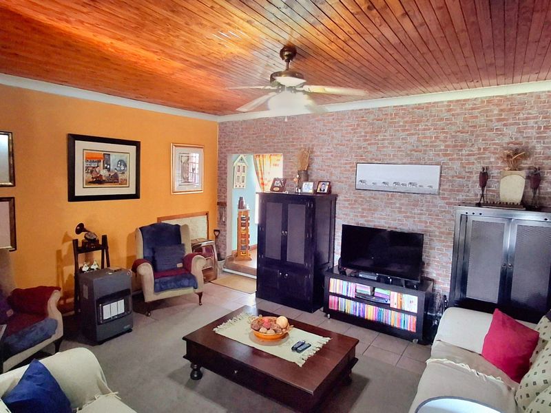 Spacious living room featuring a warm timber tongue and groove ceiling, an exposed brick feature wall, and neutral tiled flooring.