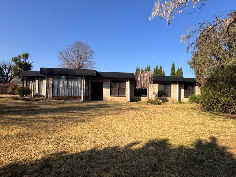 A single-story brick residence featuring a flat roof, security bars on windows, and a spacious, established lawn area.