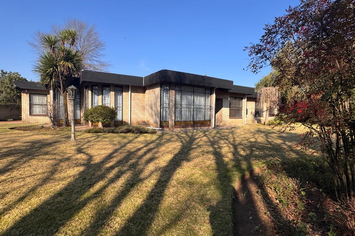 A view of the rear brick facade of the house, featuring large windows with security bars and a well-maintained garden area.
