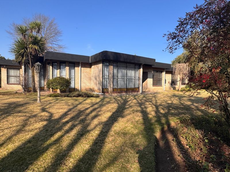 A view of the rear brick facade of the house, featuring large windows with security bars and a well-maintained garden area.