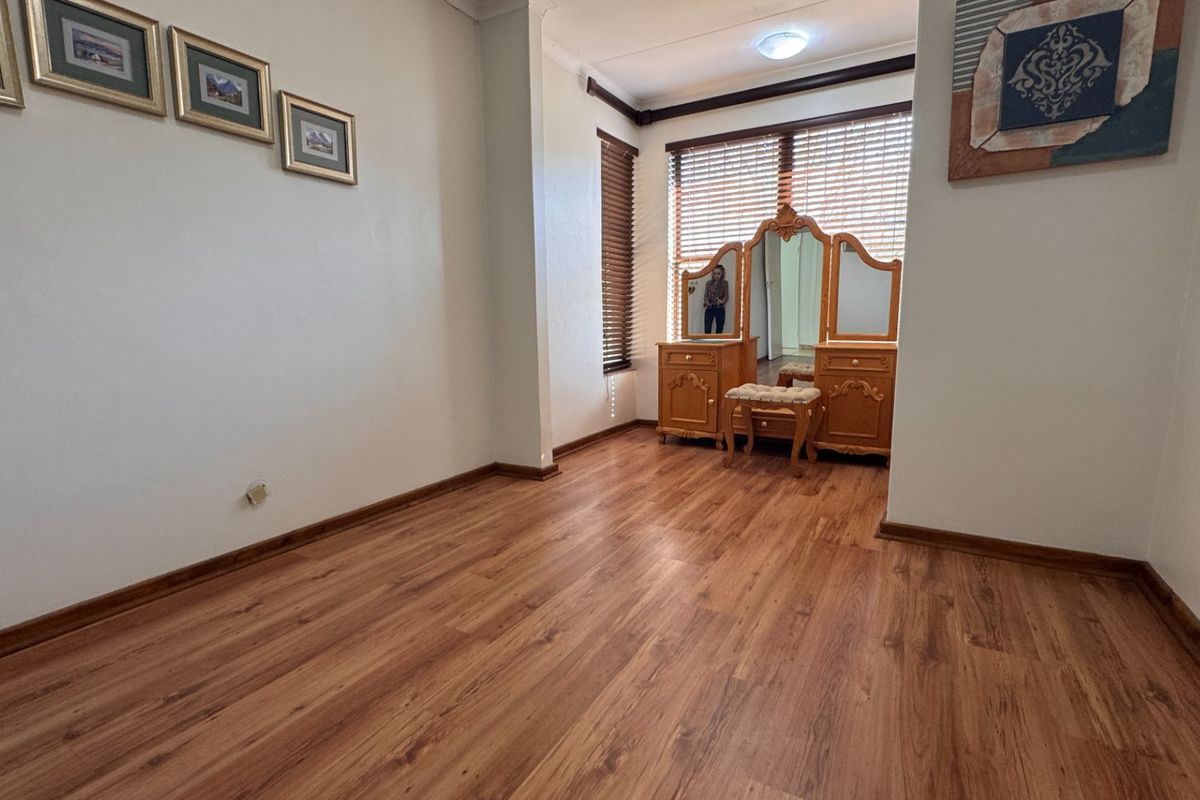 A bright, empty bedroom featuring warm-toned laminate flooring, neutral walls, and timber venetian blinds, offering a clean canvas for personalization.