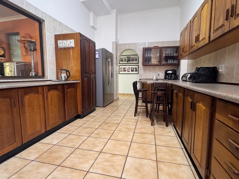 A functional kitchen featuring extensive wooden cabinetry, laminate countertops, and ceramic floor tiles, with an open archway leading to adjacent living spaces.