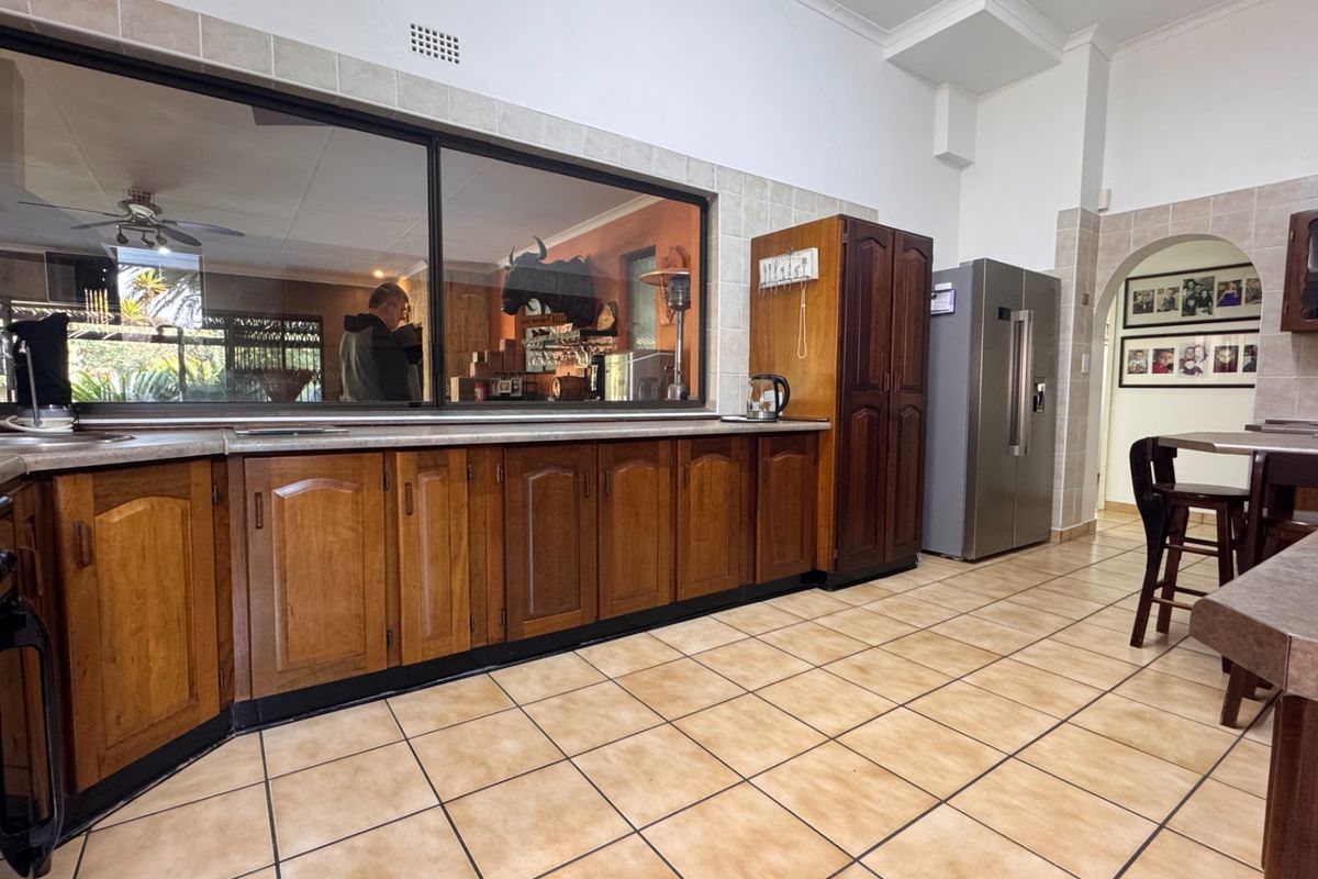 Spacious kitchen featuring traditional wooden cabinetry, tiled flooring, and a large serving window connecting to an adjacent living area.