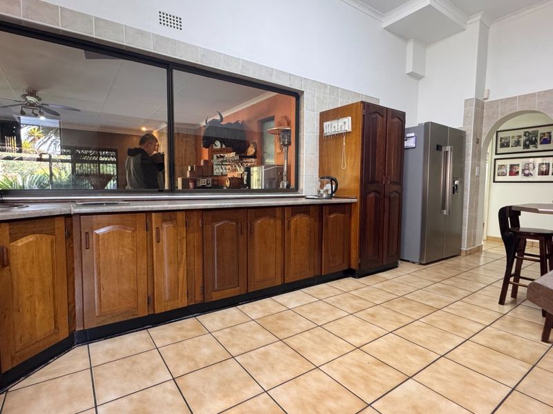 Spacious kitchen featuring traditional wooden cabinetry, tiled flooring, and a large serving window connecting to an adjacent living area.