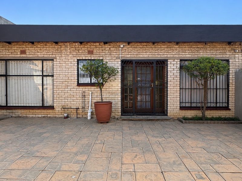 A well-maintained rear exterior featuring a face brick facade, paved patio area, and secure window and door treatments.