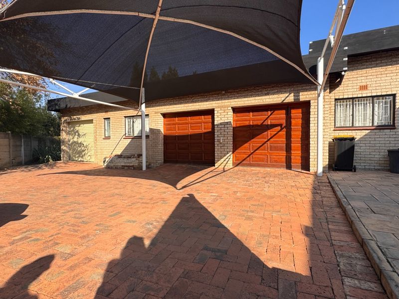 Front exterior view featuring a paved driveway, a large shade sail, and multiple garage doors with a face brick finish.