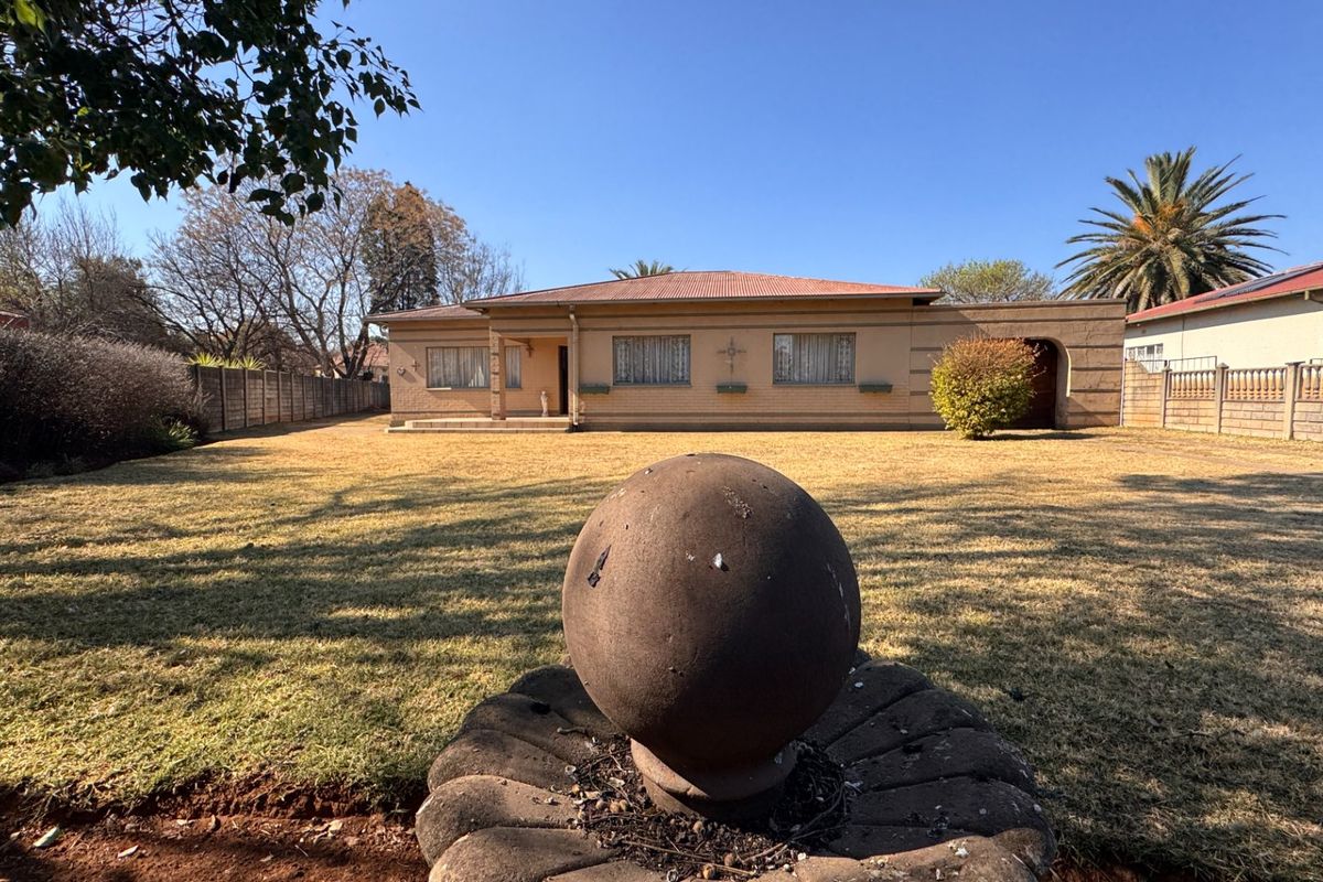 A view of the rear exterior of the house featuring a brick facade, corrugated roof, and a large garden with a stone water feature.