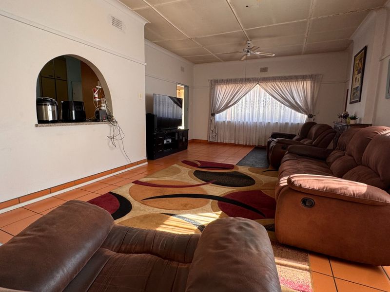 Spacious living room featuring tiled flooring, a ceiling fan, and a decorative archway connecting to the kitchen area.