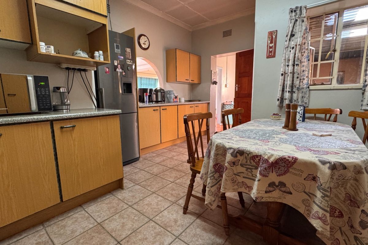 A functional kitchen featuring laminate cabinetry, tiled flooring, and an open-plan dining area, offering a practical layout with potential for modern cosmetic updates.