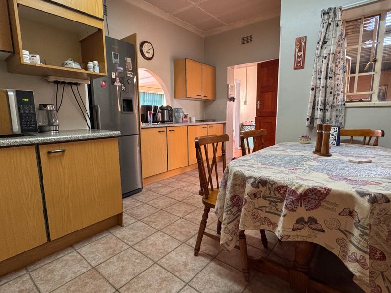 A functional kitchen featuring laminate cabinetry, tiled flooring, and an open-plan dining area, offering a practical layout with potential for modern cosmetic updates.