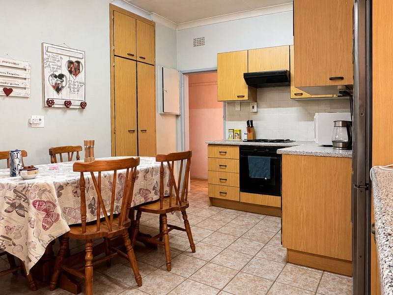 Open-plan kitchen and dining area featuring dated wooden cabinetry, gas hob, oven, extractor fan, and tiled flooring.