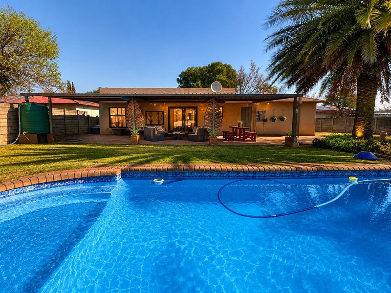A well-maintained backyard featuring a sparkling swimming pool, a spacious covered patio area, and a landscaped garden with a boundary wall.