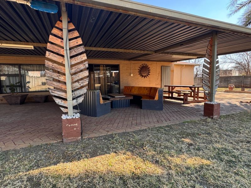 A covered outdoor patio area featuring brick paving, corrugated metal roofing, and direct access to the home through sliding glass doors.