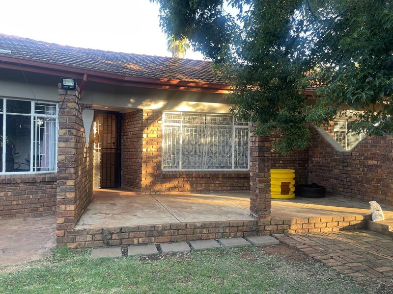 Front elevation of a face brick house featuring a covered patio entrance, tiled roof, and security fixtures on windows and doors.