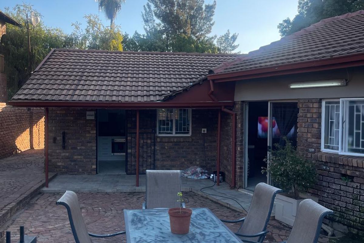 Rear exterior view of the house featuring a paved patio area, brick facade, and tiled roof structure.
