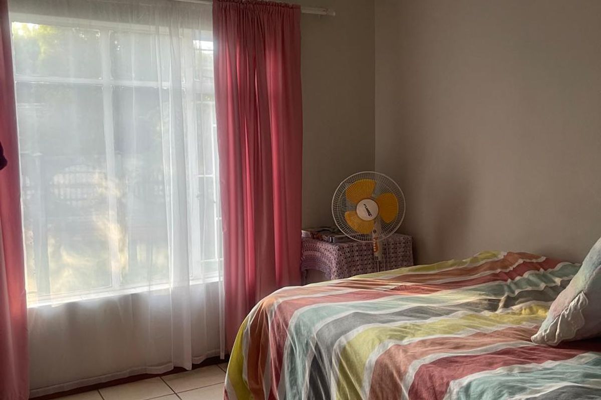 A bedroom featuring tiled flooring and a large window with curtain fittings, providing natural light.